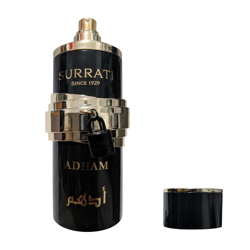 A black cylindrical perfume bottle with gold lettering reading 'Surrati Since 1929' and 'Adham', featuring shiny gold metallic bands, a small black lock, and an Arabic word. The cap is placed beside the bottle on a plain white background.