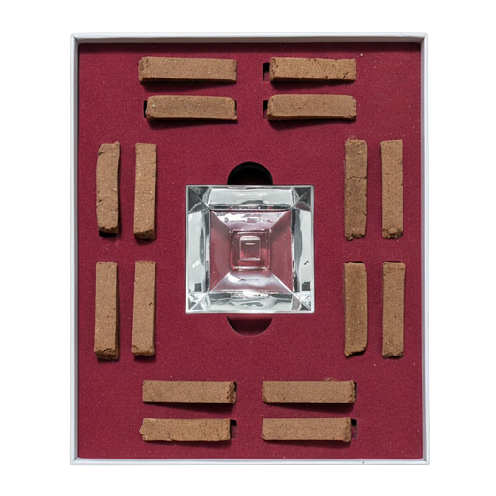 A square glass perfume atomizer bottle displayed in a red velvet-lined box with eight brown incense sticks arranged around it.