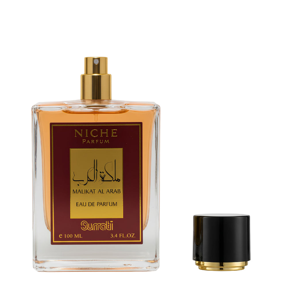 A clear rectangular perfume bottle filled with amber liquid, featuring a gold spray top and a front label with gold and dark red text. The cap is placed beside the bottle on a plain white background.
