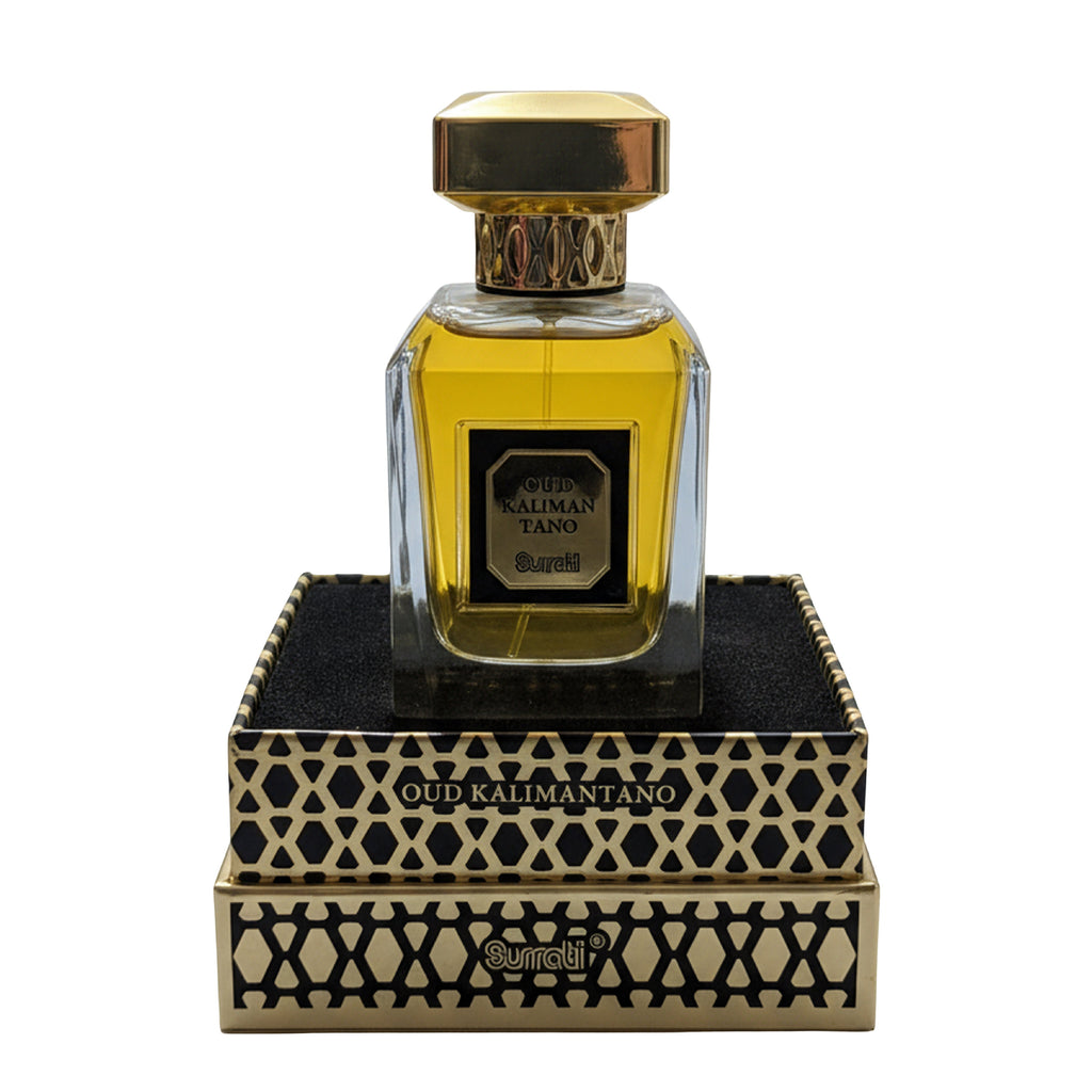 A bottle of Oud Kalmantang perfume by Gurnei, featuring a clear glass bottle filled with golden-yellow liquid and topped with a gold cap, displayed on top of its ornate black and gold patterned presentation box against a white background.