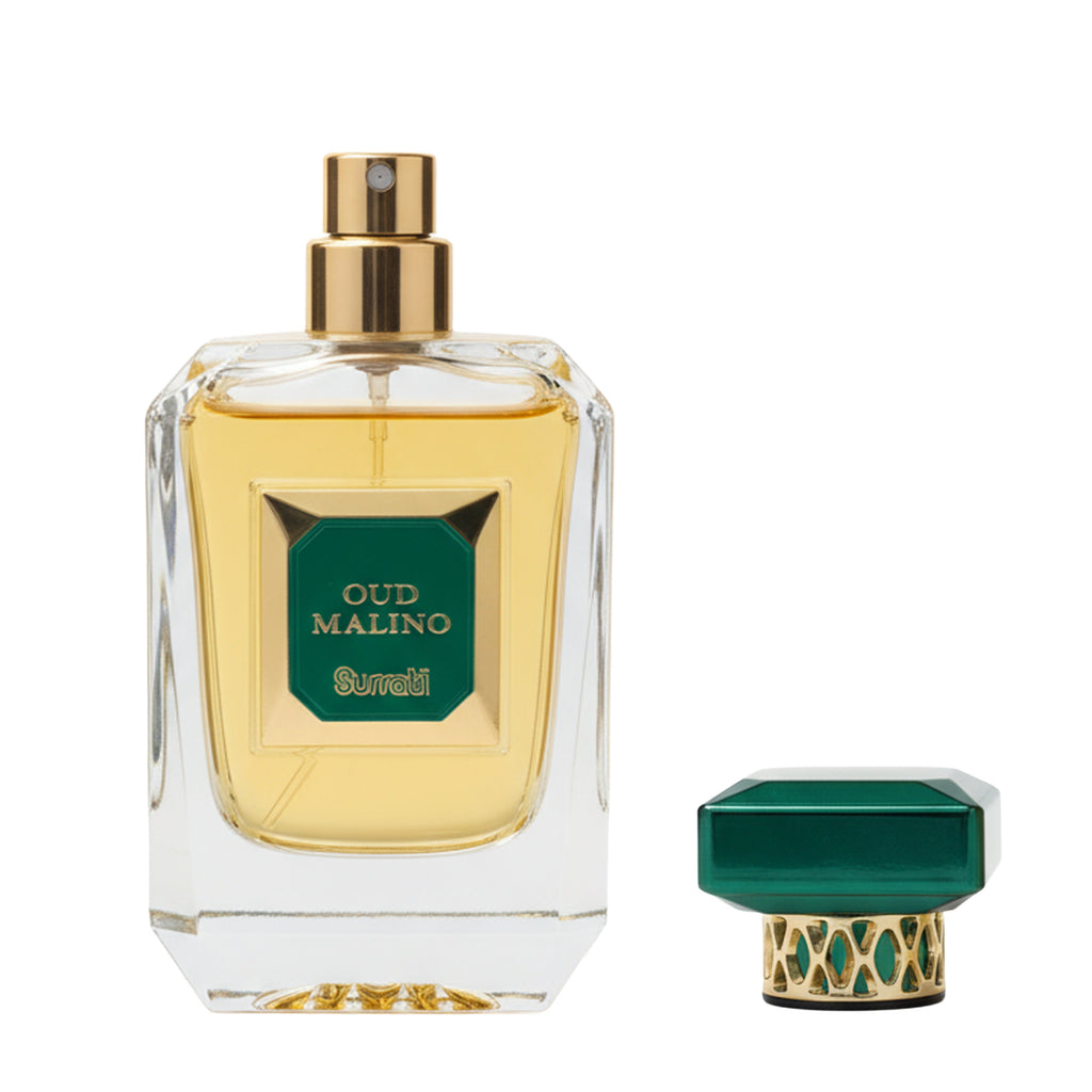 A clear glass perfume bottle filled with pale yellow liquid, featuring a gold spray top and a green front label that reads 'OUD MALINO' and 'Surrati'. A matching green-and-gold cap is shown beside the bottle on a white background.