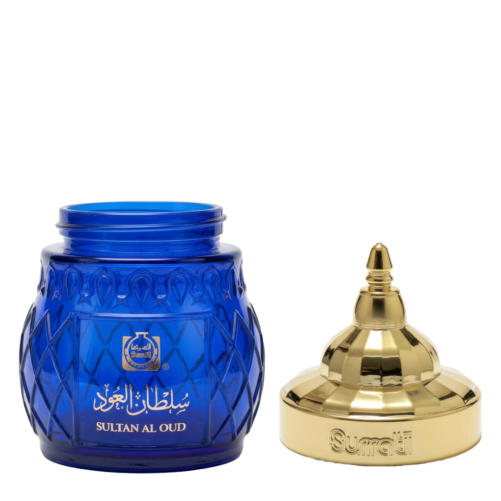 A blue glass perfume jar with a textured diamond pattern and Arabic branding, shown next to its ornate gold metal cap on a white background.