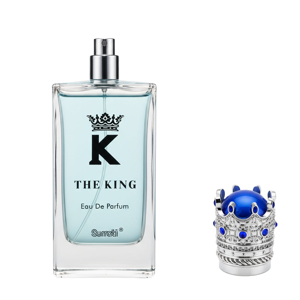 A clear rectangular perfume bottle labeled 'K THE KING' with a silver spray top, shown beside a small silver crown cap with a blue jewel-like top. The bottle contains a pale blue liquid and the brand name 'Sureti' is visible near the bottom.