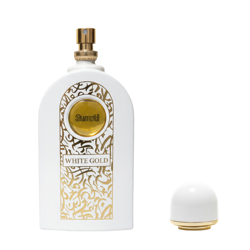 A white perfume bottle with gold Arabic calligraphy detailing and a gold spray nozzle, shown next to its white and gold cap on a plain white background. The label reads 'Surati' and 'WHITE GOLD'.